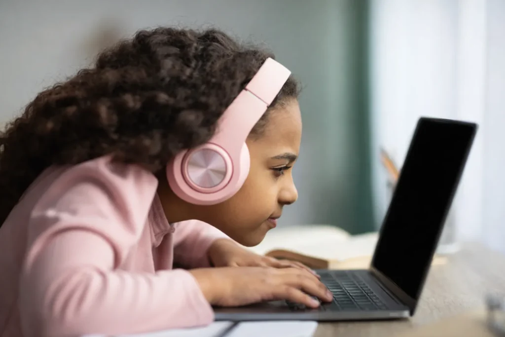Niña usando computadora portátil con postura de problemas de visión, señal común de problemas visuales infantiles como fatiga ocular y dificultad para concentrarse.